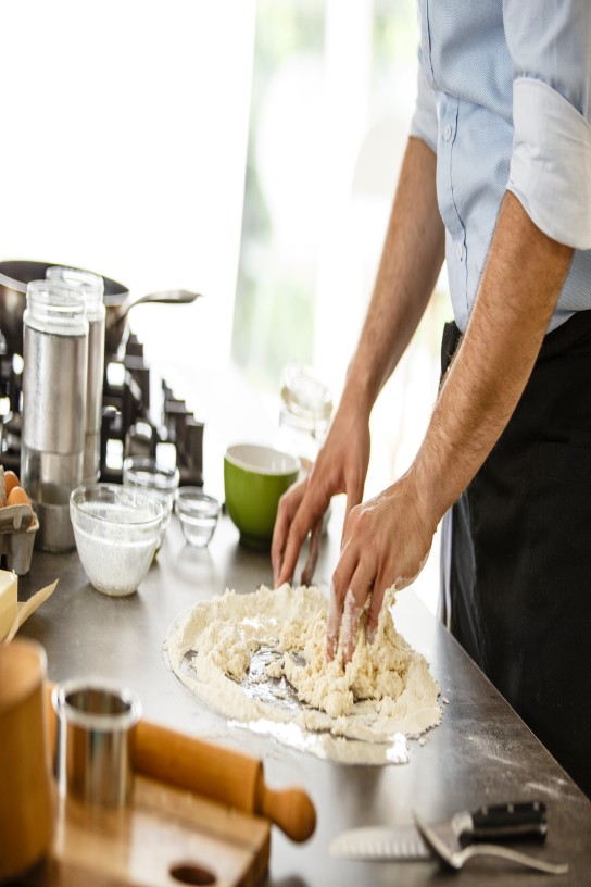 Mid adult man with black apron baking pizza dough in the kitchen.