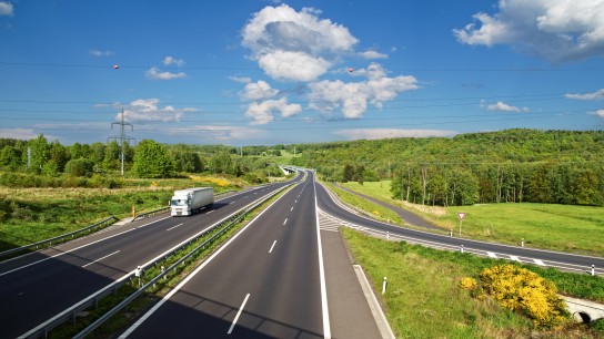 Access road to the asphalt highway between forests and fields